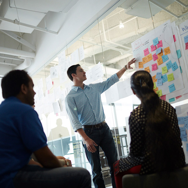 Man pointing to notes on a board while two other people watch.