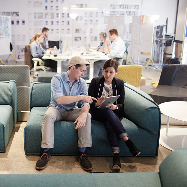 Two people sitting on a couch, looking at a tablet.