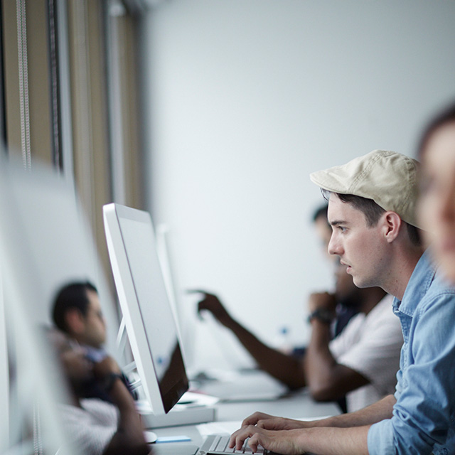 People sitting at a desk while looking at their computer monitors.