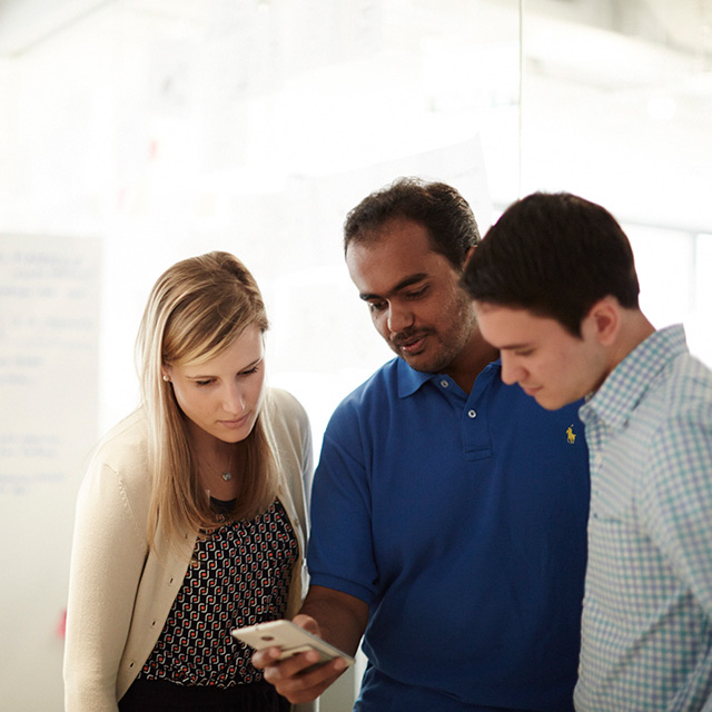Three people looking at a mobile phone.