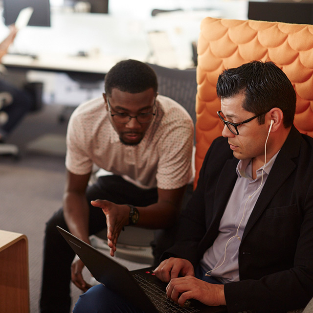 Two people sitting on a couch looking at a laptop.