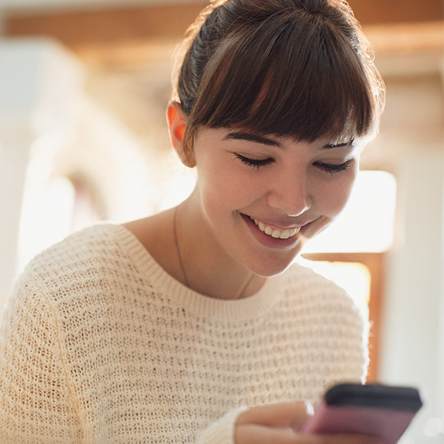 Woman smiling at her phone and making a payment on her device. 